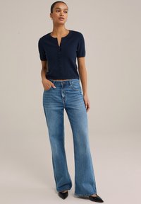 Tumed lühikeste varrukatega nööbiga ülaosa, millele onpaaritud helesinised laiad teksad ja mustad terava ninaga kingad. Sile tekstuur ja klassikalised disainielemendid.