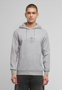 Hanorac gri cu buzunar frontal și glugă cu șnur. Prezintă un logo grafic verde cu palmieri pe piept. Croi casual și textură.