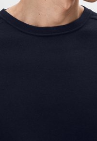 Pull à col rond bleu marine avec texture côtelée et coupe classique. Présente des coutures discrètes sur les épaules, fabriqué en tissu doux.