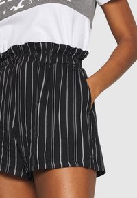 Černobílé pruhované šortky s nařaseným elastickým pasem a bočními kapsami. Vyrobené z lehkého materiálu, mají uvolněný střih.
