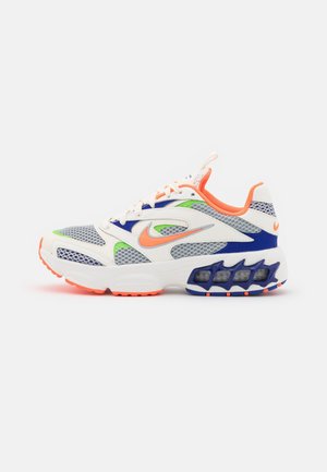 Chaussure de sport blanche avec des accents orange, bleu et vert, panneaux en mesh, semelle rembourrée et unités de coussin d'air visibles.