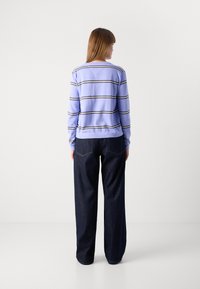 Pull rayé lilas clair avec des rayures horizontales blanches et noires, associé à un jean denim foncé à jambes larges. Texture lisse, coupe décontractée.