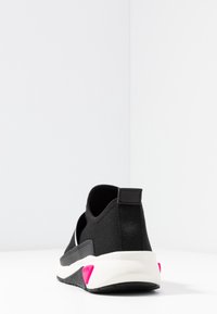 Mustat liukujalkineet, joissa on hengittävä tekstiili yläosa, valkoinen välipohja ja vaaleanpunaiset kantapääkoristeet. Iskunvaimentava kumipohja.