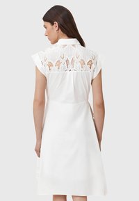 Weißes Kleid mit kurzen Ärmeln, einem kragenförmigen Ausschnitt und einem Rückenpaneel aus Spitze mit Blumenmustern. Glatter Stoff und A-Linie Silhouette.