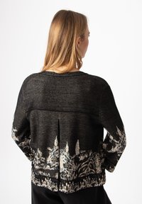 Čierny sveter s textúrovaným povrchom a bielou potlačou inšpirovanou prírodou na dolnom leme, s detailom záševku na chrbte.