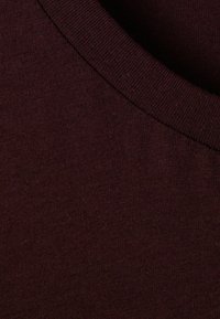Tă fabrică de bumbac burgund cu o textură netedă. Prezintă un gât rotund ribetat și un model subtil heathered pe toată suprafața.