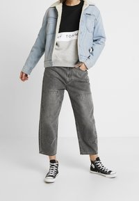 Chaqueta de mezclilla azul claro con cuello de borreguillo, sudadera gris y pantalones cargo grises holgados, combinados con zapatillas altas negras.
