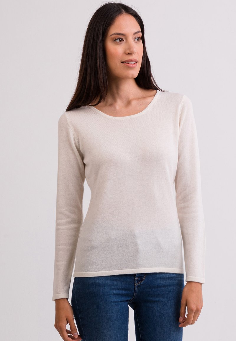 Helle beige Langarmbluse aus weichem Material, mit einem runden Halsausschnitt und dezentem Muster, kombiniert mit dunkelblauen Jeans.