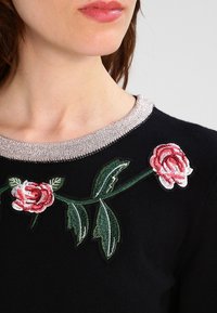 Maglione nero con colletto argentato testurizzato e ricami floreali in rosa e verde, con dettagli di foglie e rose sulla scollatura.