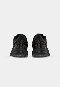 Bottes de sport noires avec un dessus texturé, un design épuré et des accents brillants sur le côté et le talon. Semelle extérieure avec motifs de traction.