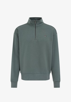 Tummanvihreä pusero puolivetoketjukauluksella, resorit helmassa ja hihansuissa, sekä pieni kirjailtu logo rinnassa. Pehmeä materiaalin rakenne.