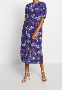 Paarse bloemenjurk met korte pofmouwen, verzamelde halslijn en een vloeiende silhouet. Heeft levendige blauwe en oranje bloemmotieven.