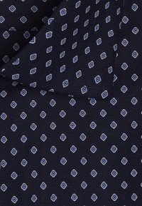 Tessuto navy con una trama testurizzata, caratterizzato da un motivo a rombi ripetuto in blu chiaro e bianco, creando un design a contrasto.
