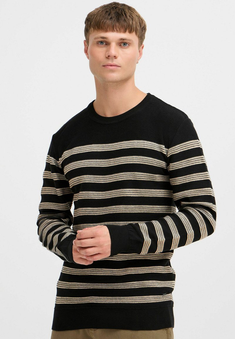 Black and cream striped sweater with a round neckline, long sleeves, and ribbed cuffs. Soft knit fabric with prominent horizontal lines.