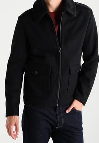 Svart zip-up jacka med en mjuk, texturerad krage, två framfickor och en figursydd design. Tillverkad av varmt, hållbart tyg.