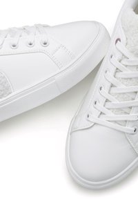 Sneakers bianchi in pelle liscia con un accento testurizzato e morbido sul lato. Presentano lacci piatti e una suola in gomma.