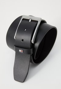 Cinturón de cuero negro con una hebilla de metal plateado. Presenta una textura suave y orificios para el ajuste. Incluye un acento de logo en la correa.