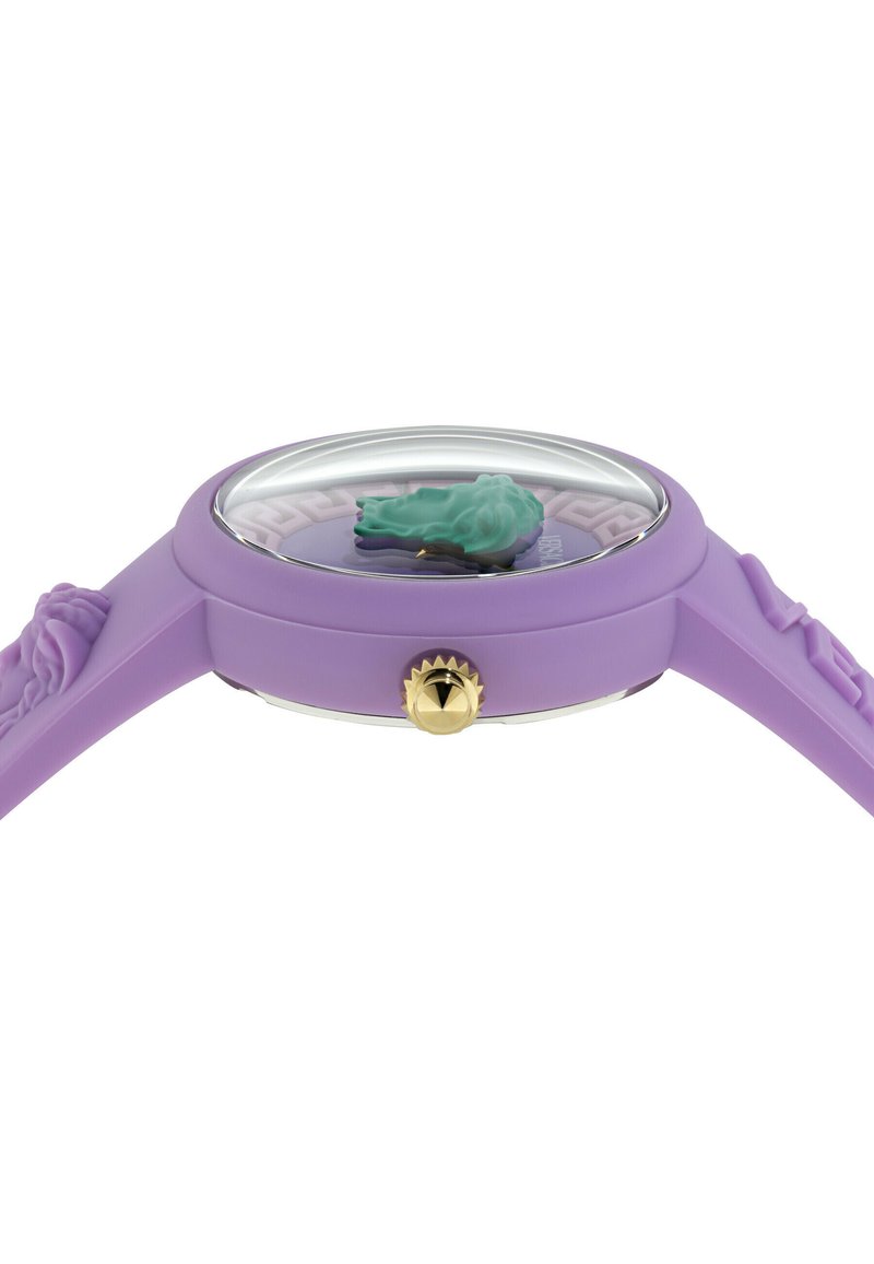 Orologio in silicone viola con cinturino testurizzato, quadrante rotondo, vetro trasparente e corona dorata. Presenta un elemento decorativo verde sul quadrante.