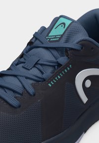 Mørkeblå sportssko med blå snørebånd, lyseblåt logo-patch på tungen og teksten "DELTASTRAP" på siden.