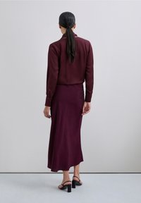 Blusa burdeos de manga larga y cuello, combinada con una falda hasta la rodilla con un patrón texturizado. Sandalias negras sencillas con tacón ancho.