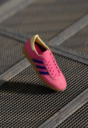 Pink sneaker with yellow accents, featuring purple stripes and textured rubber sole. Lightweight upper and flat laces for secure fit.