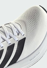 Zapatilla deportiva blanca con parte superior de malla y acentos sintéticos negros, que cuenta con una suela texturizada y un detalle "DREAMSTRIKE" en el lateral.
