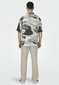 Korte mouwen shirt in abstracte grijs en zwarte patronen, gemaakt van lichte stof, gedragen met losse beige broek en sneakers.