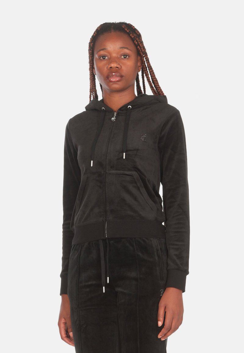 Felpa nera in velluto con zip, dotata di tasca frontale, polsini a coste e cappuccio con coulisse. Presenta un piccolo logo sul petto. Texture morbida.