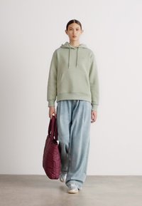 Lys grønn hettegenser med frontlomme, kombinert med løse lys blå jeans. Holder en bordeauxfarget quiltet totebag, med sølvfargede sneakers.