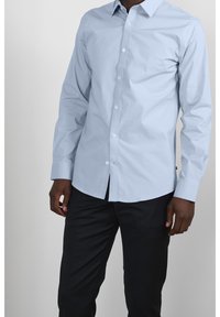 Ljusblå långärmad skjorta i bomull med knappad krage, framplacket och justerbara manschetter. Matchas med svarta byxor.