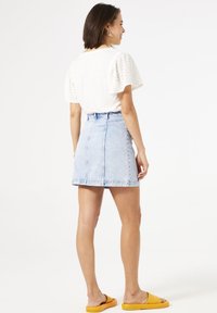 Weißes Oberteil mit Puffärmeln und Lochstickereien, kombiniert mit einem hellblauen Denim-Minirock. Das Model trägt gelbe Slipper.