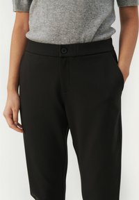 Black trousers made of smooth fabric, featuring a button closure, side pockets, and a tailored fit. Simple design with no visible patterns.
