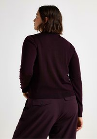 Mørk burgunder strikket sweater med rund halsudskæring og lange ærmer. Har ribbet kant og ryg, parret med matchende højtaljede bukser.