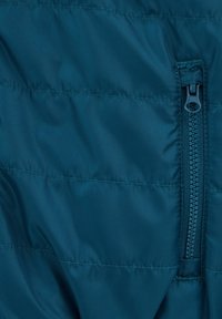 Turkos puffjacka i tyg med en vertikal dragkedjeficka. Materialet är slätt och glänsande, med kviltade sömmar för isolering.