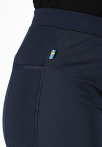 Leggings performanti color navy con un ampio elastico in vita, texture liscia e un piccolo accento della bandiera svedese vicino alla tasca posteriore.