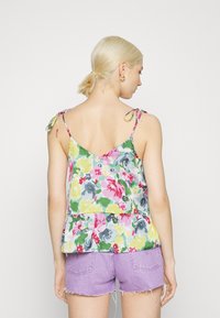 Top de flores em cores pastéis com um design peplum e alças de laço. O tecido apresenta uma mistura de padrões em rosa, verde e amarelo.