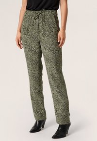 Groene panterprintbroek met een elastische tailleband en een trekkoord, gemaakt van een lichte stof, gecombineerd met zwarte hakken enkellaarzen.