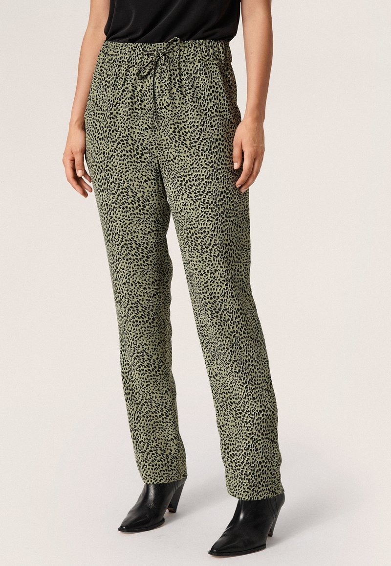 Groene panterprintbroek met een elastische tailleband en een trekkoord, gemaakt van een lichte stof, gecombineerd met zwarte hakken enkellaarzen.