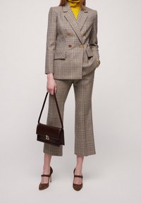 Dubbelknäppt rutigt blazer i beige och svart, kombinerat med rutig byxa med vida ben. En gul polotröja under och en brun handväska.