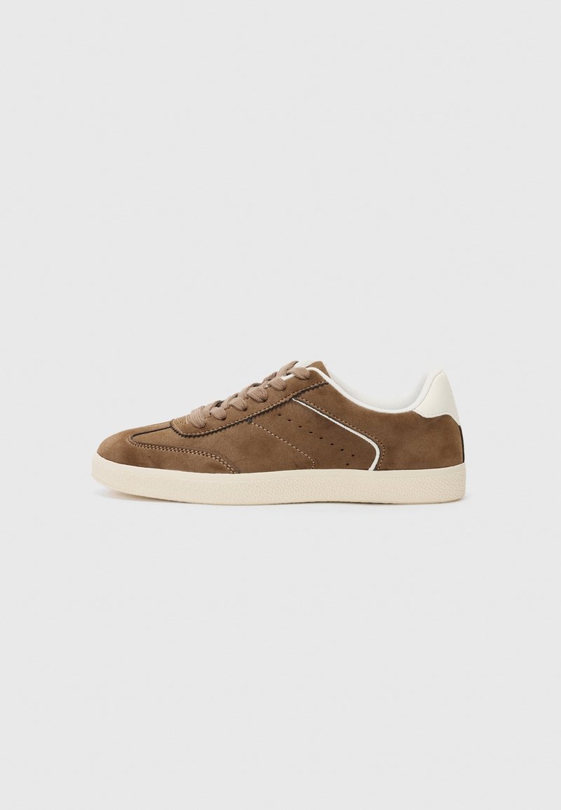 Baskets basses en daim marron avec semelle beige, lacets beiges, accent blanc au talon et détails de perforation sur le côté.
