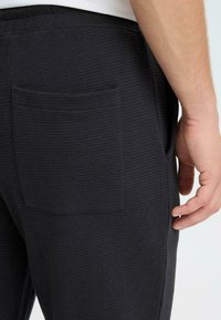 Ciemnoszare, teksturowane spodnie dresowe z boczną kieszenią. Tkanina ma wzór waflowy, a pas jest elastyczny dla wygody.