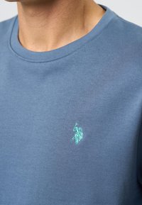 Mannen blauwe rondhals t-shirt van katoen. Bevat een subtiele geborduurde logo in lichtgroen op de linkerborst. Soepele textuur.
