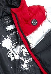 Veste matelassée rouge, blanche et noire avec zipper noir, patch logo rond et doublure intérieure noire présentant un graphique de skull blanc et une étiquette de marque avec un tag de nom.