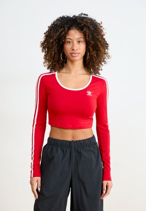 Top corto a maniche lunghe rosso con strisce bianche lungo le maniche e scollatura rotonda, abbinato a pantaloni neri con vita elastica.