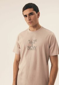 Jasnoróżowa bawełniana koszulka z czarnym nadrukowanym napisem z przodu. Klasyczny okrągły dekolt i krótkie rękawy.