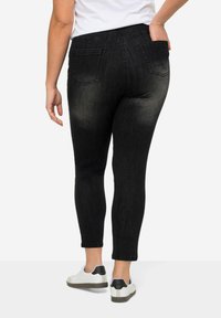 Jeans negros ajustados con efecto desgastado, con bolsillos traseros y una cintura alta. Combinados con zapatos blancos con un acento negro.