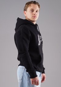 Schwarzer Hoodie mit Kängurutasche, gerippten Bündchen und verstellbaren Kordeln, kombiniert mit hellblauen Jeans.