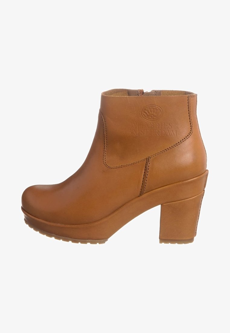 Botín de cuero color tan con puntera redonda, tacón grueso y detalle de logo en relieve. Textura suave y cremallera lateral para facilitar el calzado.