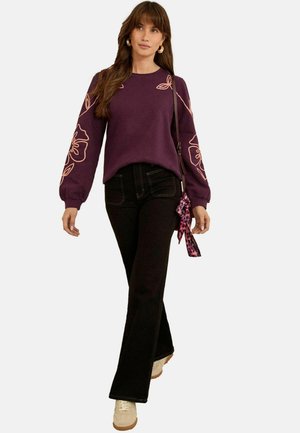 Purple sweatshirt with floral embroidery on sleeves, paired with black flared jeans and beige sneakers. Includes a patterned bag accessory.