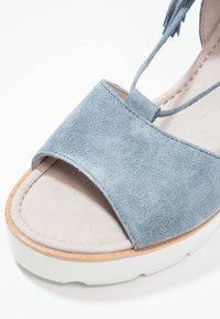 Blue suede wedge sandal with open toe design, soft beige inner lining, white rubber sole, and thin lacing detail.